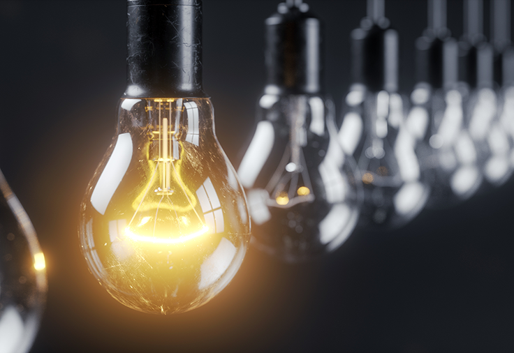 A row of light bulbs in fixtures hanging upside-down from cords. The coil in the front-most bulb is glowing.